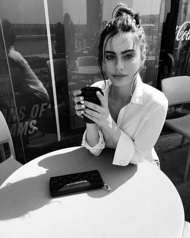 a woman sitting at a table with a cell phone in her hand and looking at the screen