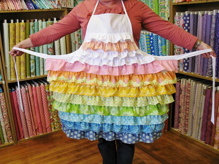 a woman wearing an apron made out of different colored fabrics in front of a bookshelf