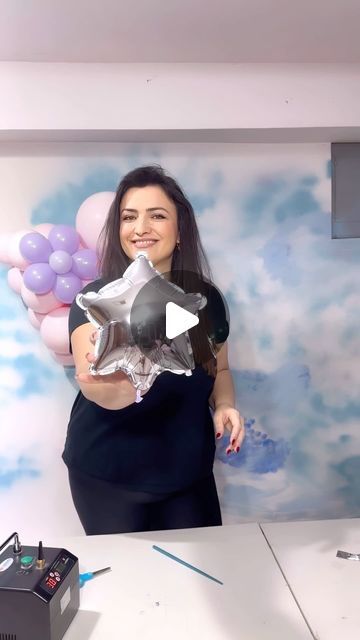 a woman is holding some balloons in front of her face while standing next to a desk