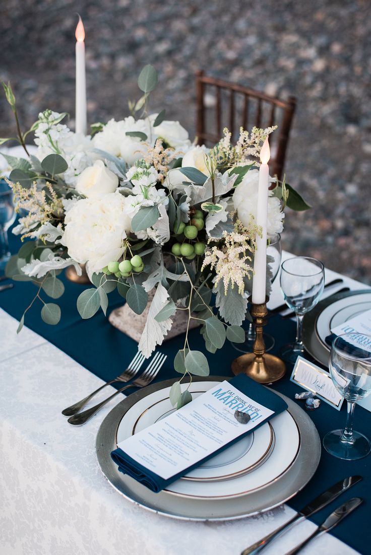 the table is set with blue and white plates, silverware, flowers, and candles