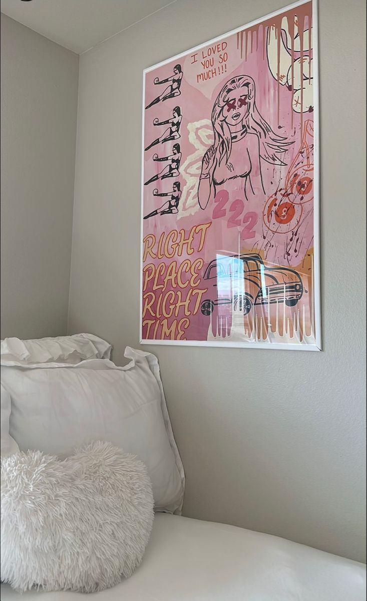 a white bed topped with pillows next to a pink painting on the wall above it