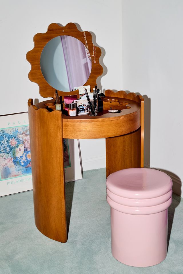 a wooden vanity table with a mirror and pink trash can on the floor next to it