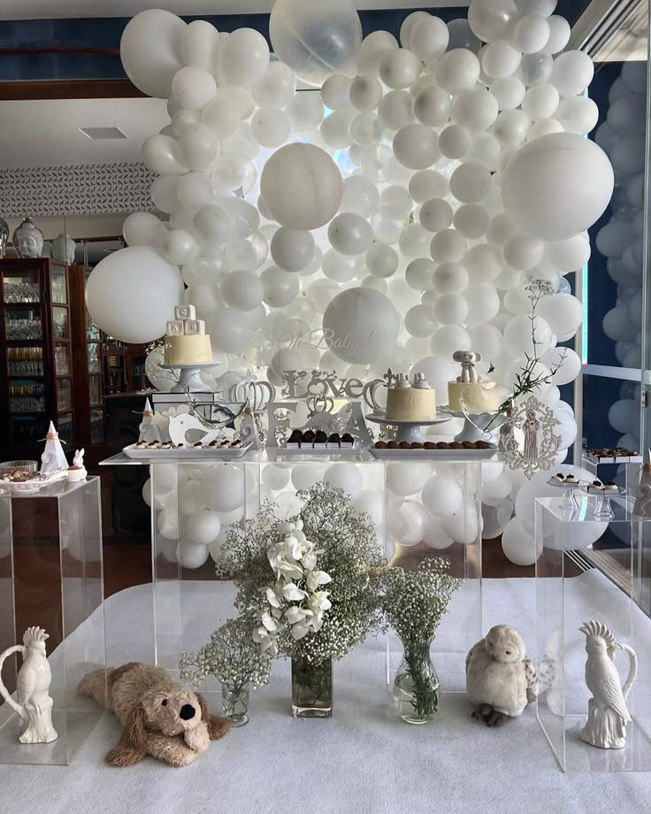 a table topped with lots of white balloons and vases filled with flowers on top of it