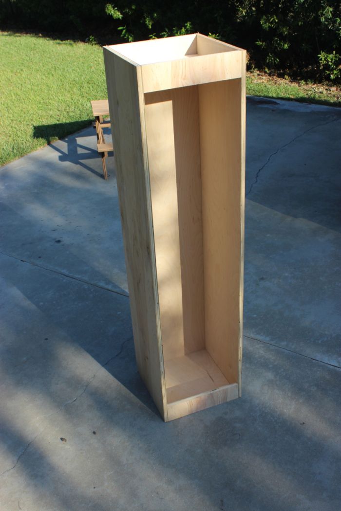 a tall wooden box sitting on top of a cement floor next to a park bench