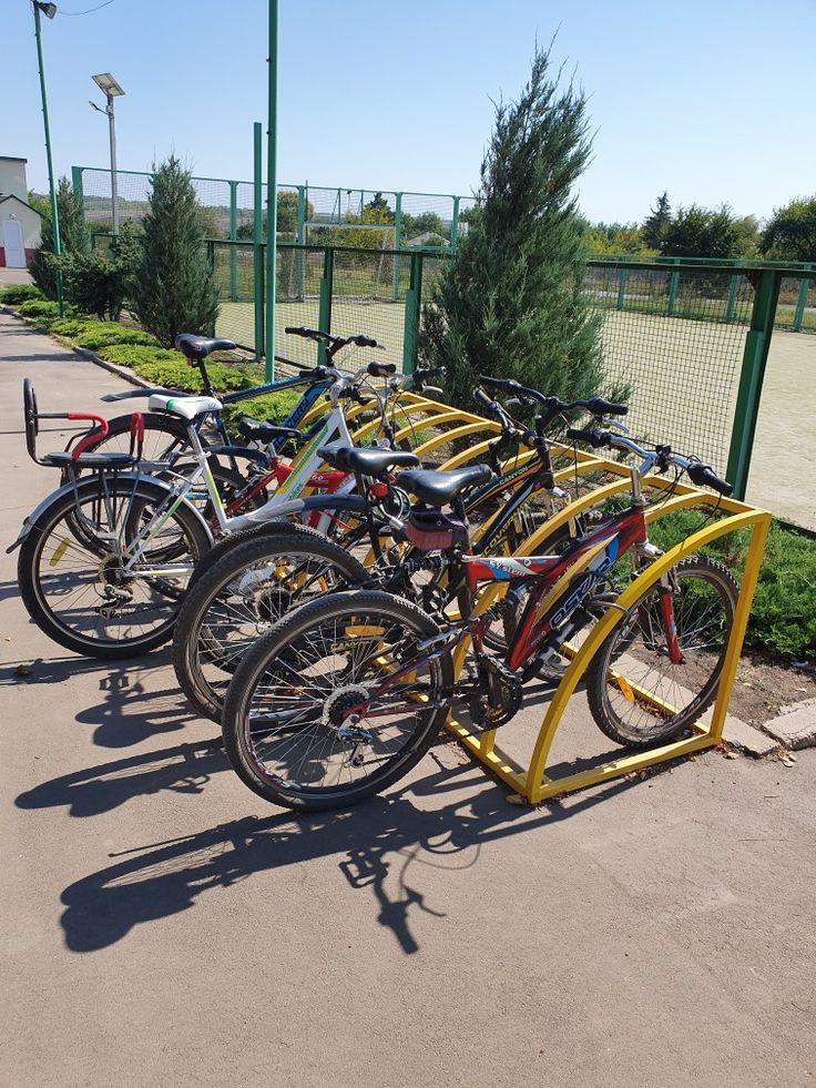 several bicycles are parked next to each other in a row on the sidewalk near a fence