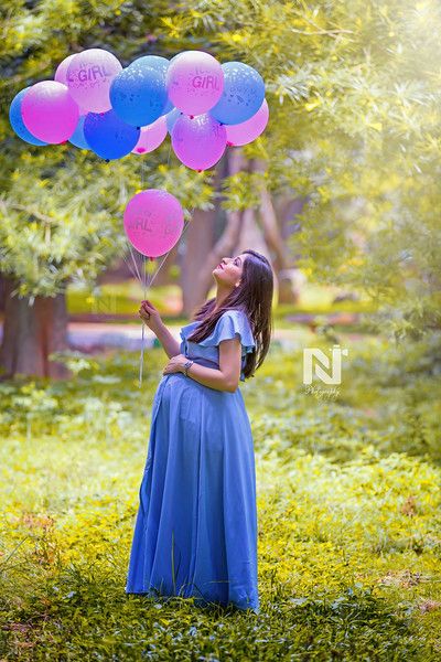 a pregnant woman in a blue dress holding pink and blue balloons