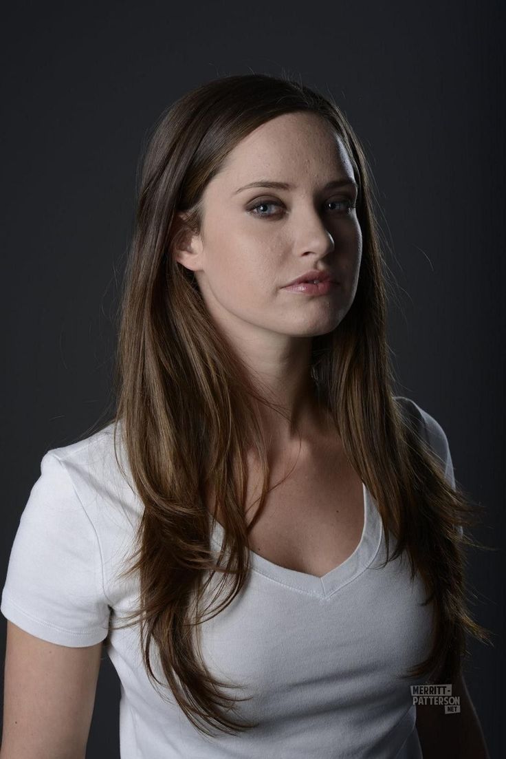 a woman with long brown hair and white shirt posing for a photo in front of a dark background