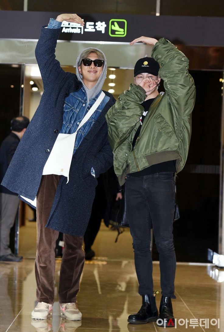 two people standing next to each other in front of an airport entrance with their arms up