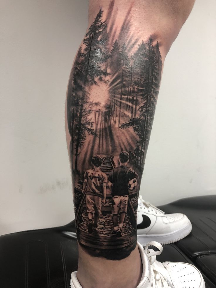 a man's leg with a black and grey tattoo on it, depicting two people walking in the woods