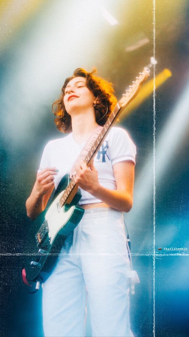 a woman holding a guitar in her hands and looking up at the sky with bright beams behind her