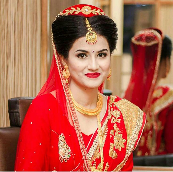 a woman wearing a red and gold bridal outfit in front of a mirror with other women in the background