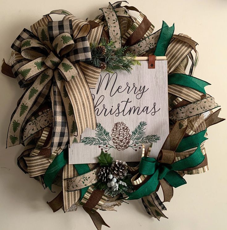 a christmas wreath hanging on the wall with ribbon and pineconis around it that says merry christmas