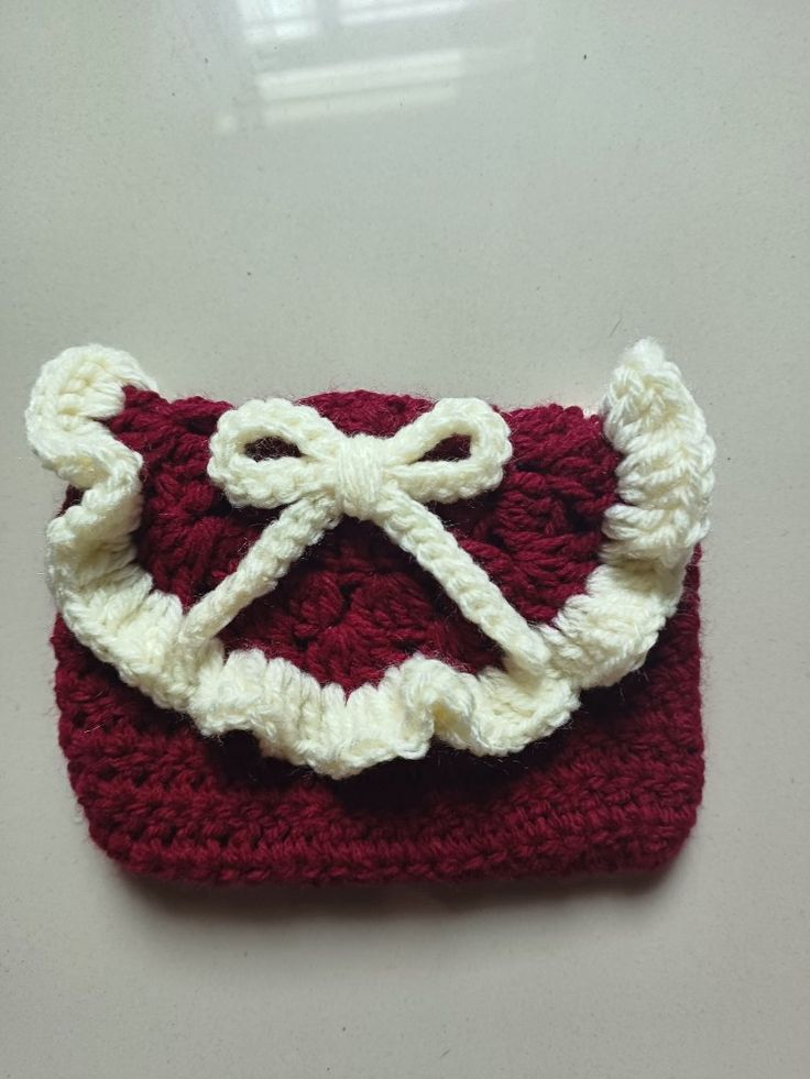 a crocheted red and white purse with a bow on the front sitting on a table