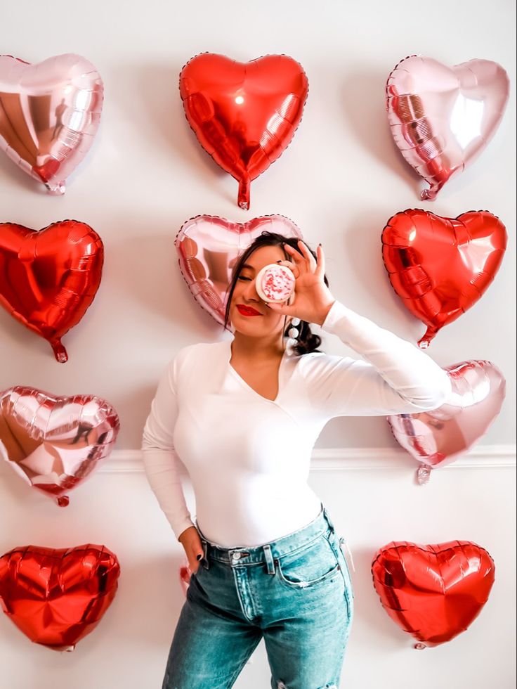 a woman standing in front of heart shaped balloons and holding a pacifier to her nose