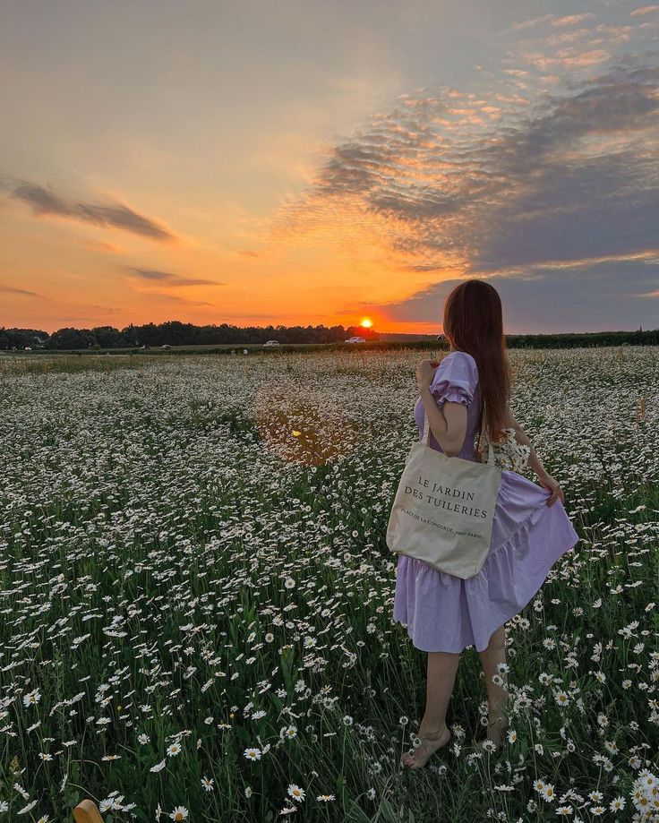 a woman walking through a field at sunset