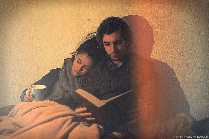 a man and woman laying in bed reading a book with a cup of coffee next to them