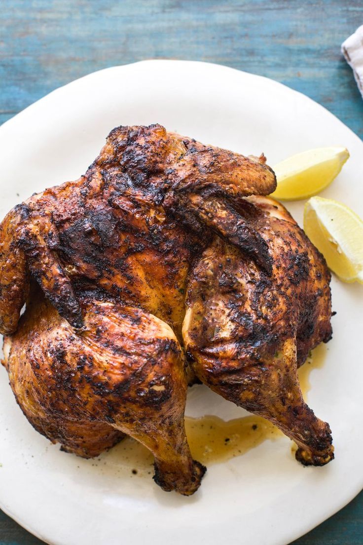 a whole chicken on a white plate with lemon wedges