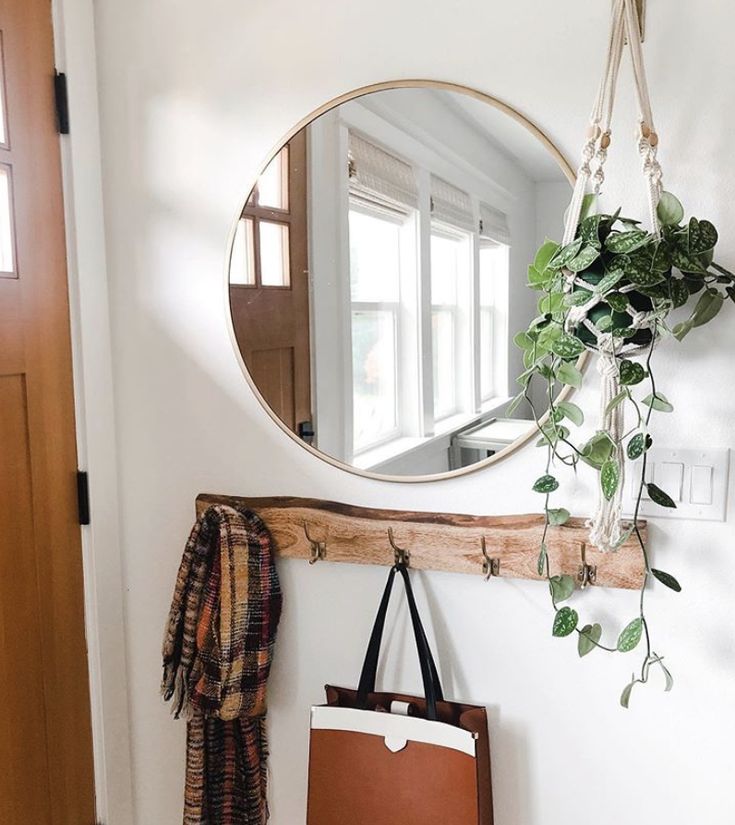 a mirror hanging on the wall next to a purse and coat rack with a plant in it