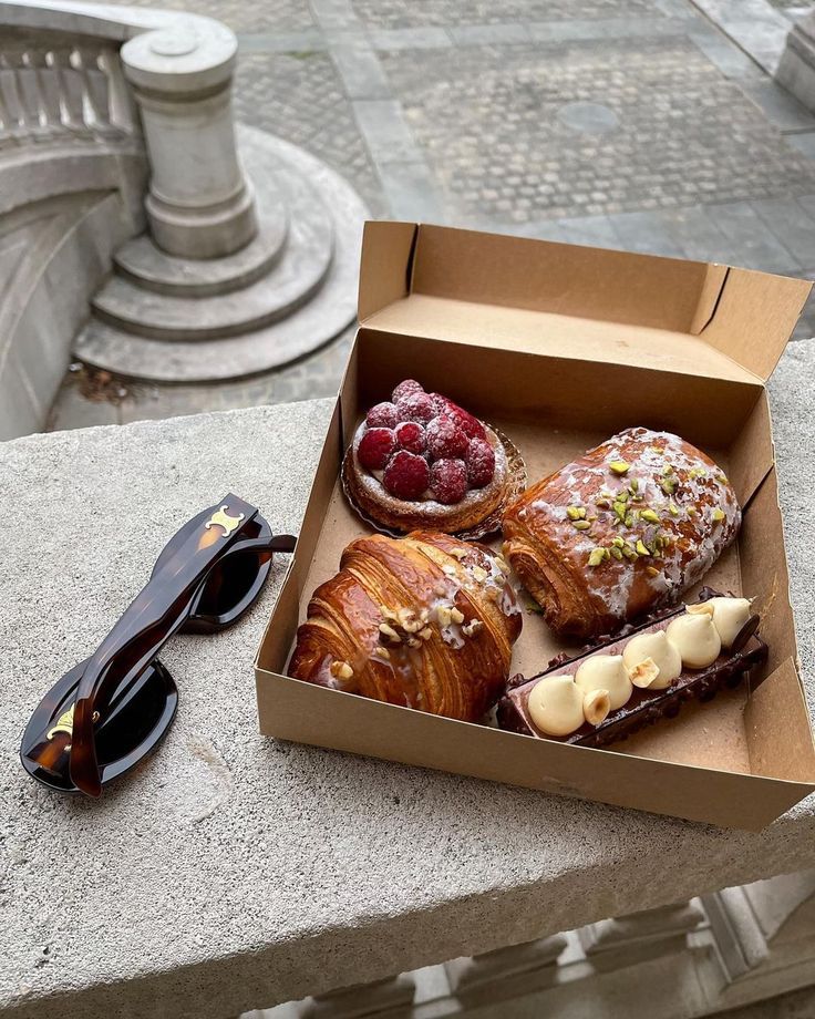 three pastries in a box with raspberries and chocolate on the table next to them