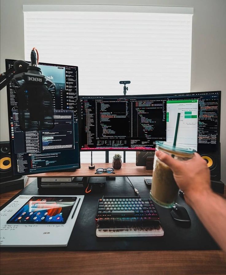 a person is holding a cup in front of two computer screens