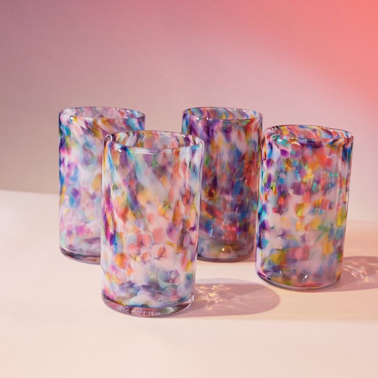 three colorful glasses sitting next to each other on a white counter top with pink and blue background