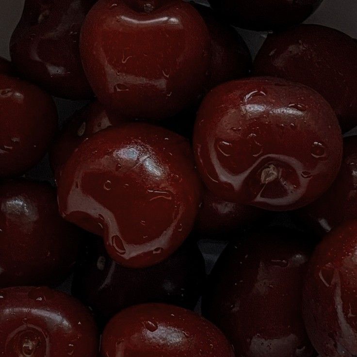 a pile of plums with water droplets on them and the top one is red