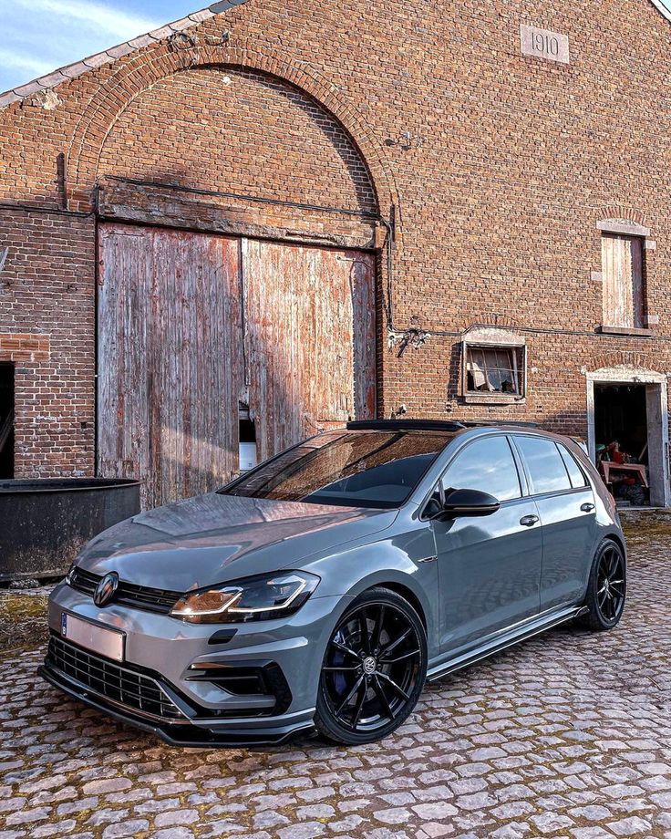 a grey car parked in front of a brick building on a cobblestone street