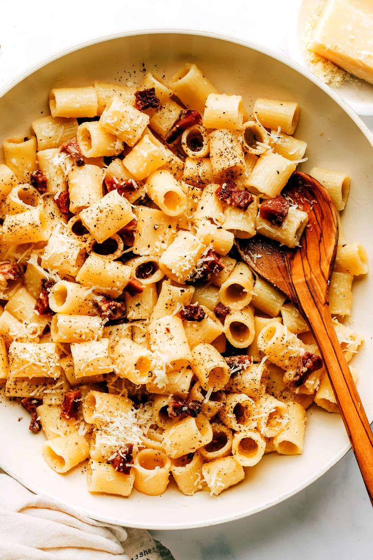 a white bowl filled with pasta and meat on top of a table next to bread