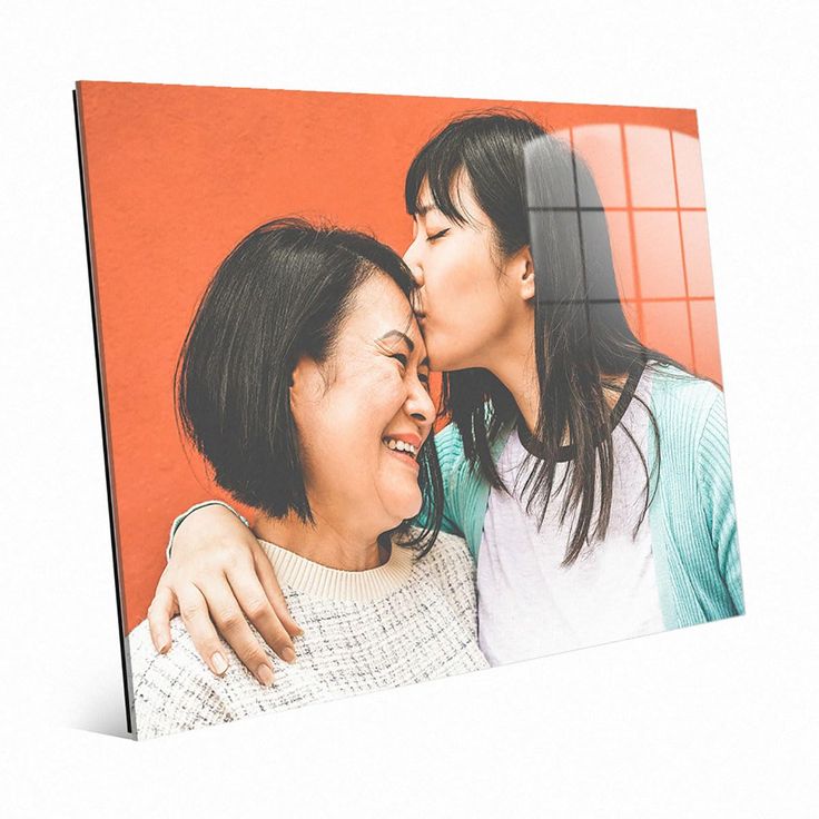 two women are kissing each other in front of an orange wall with red tiles on it