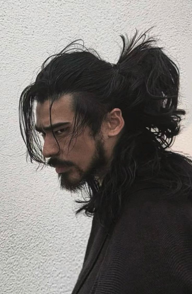 a man with long hair and a beard standing in front of a white wall