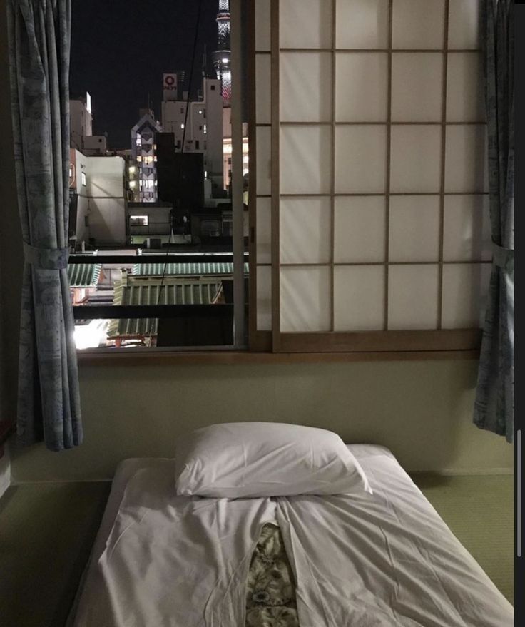 an unmade bed sitting in front of a window with city lights on the other side