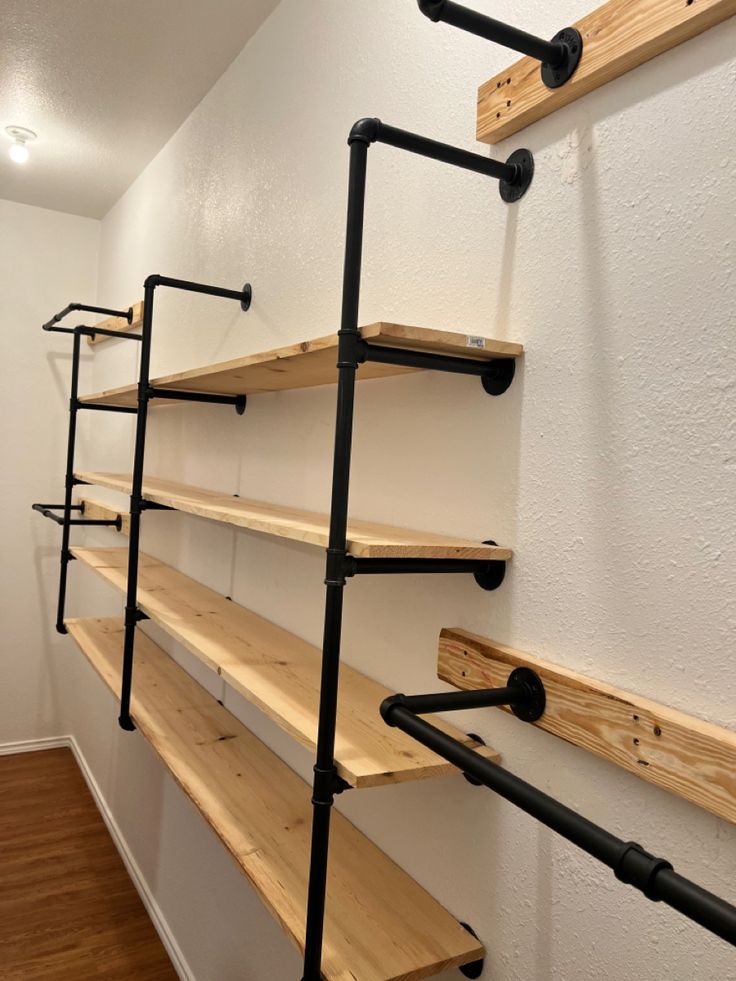 some shelves are lined up against the wall with black pipe and wood brackets on them