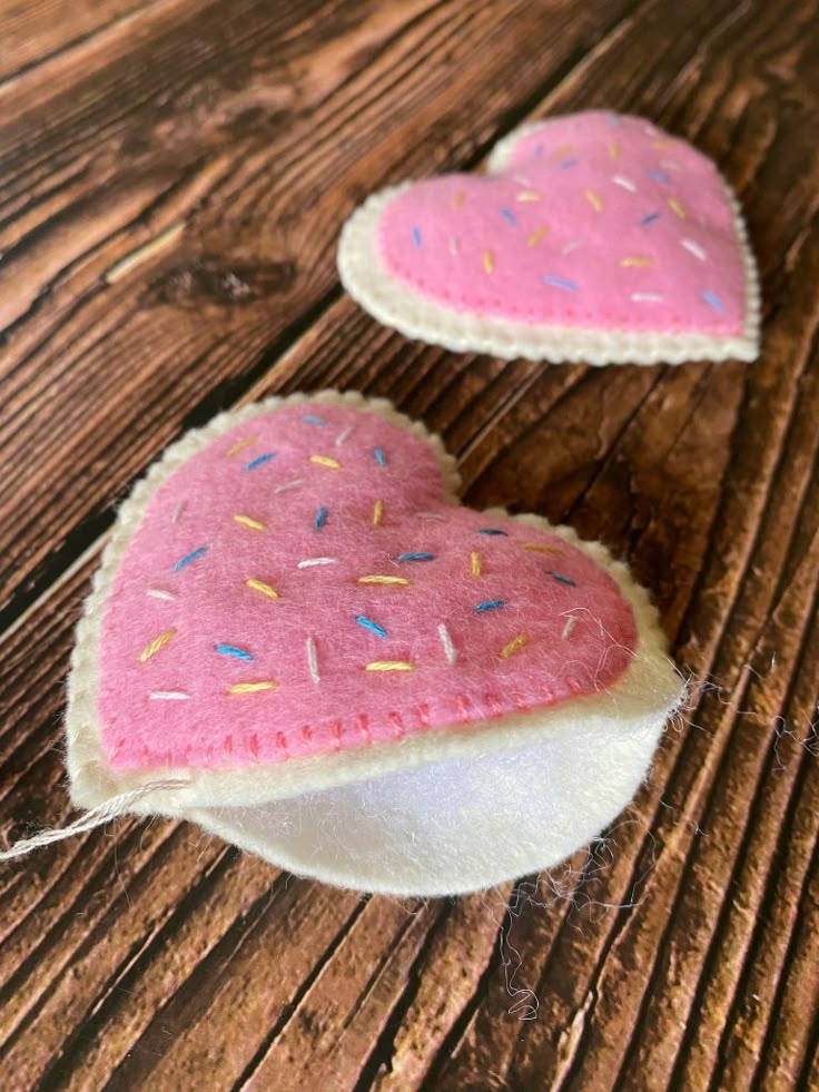 two pink heart shaped cushions sitting on top of a wooden table with sprinkles