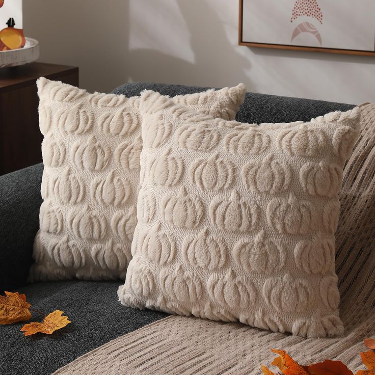 two decorative pillows on a couch with autumn leaves