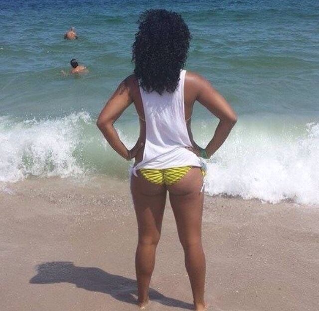 a woman standing on top of a sandy beach next to the ocean with her back turned