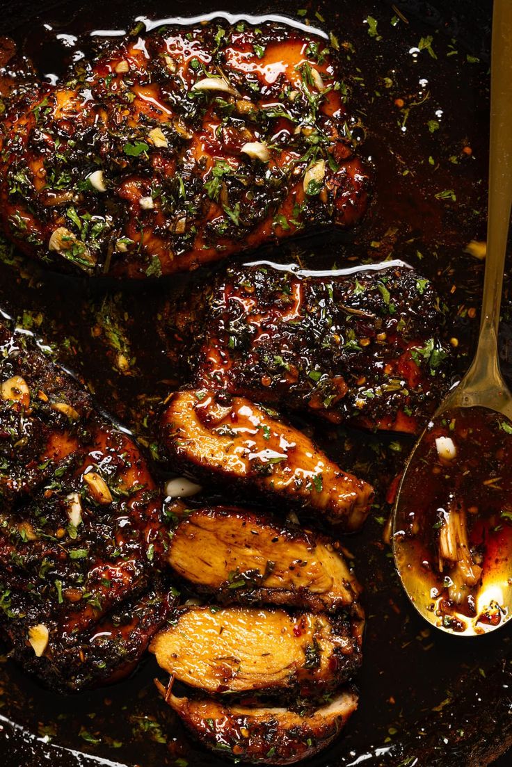 grilled pork chops with sauce and herbs on a black plate next to a spoon