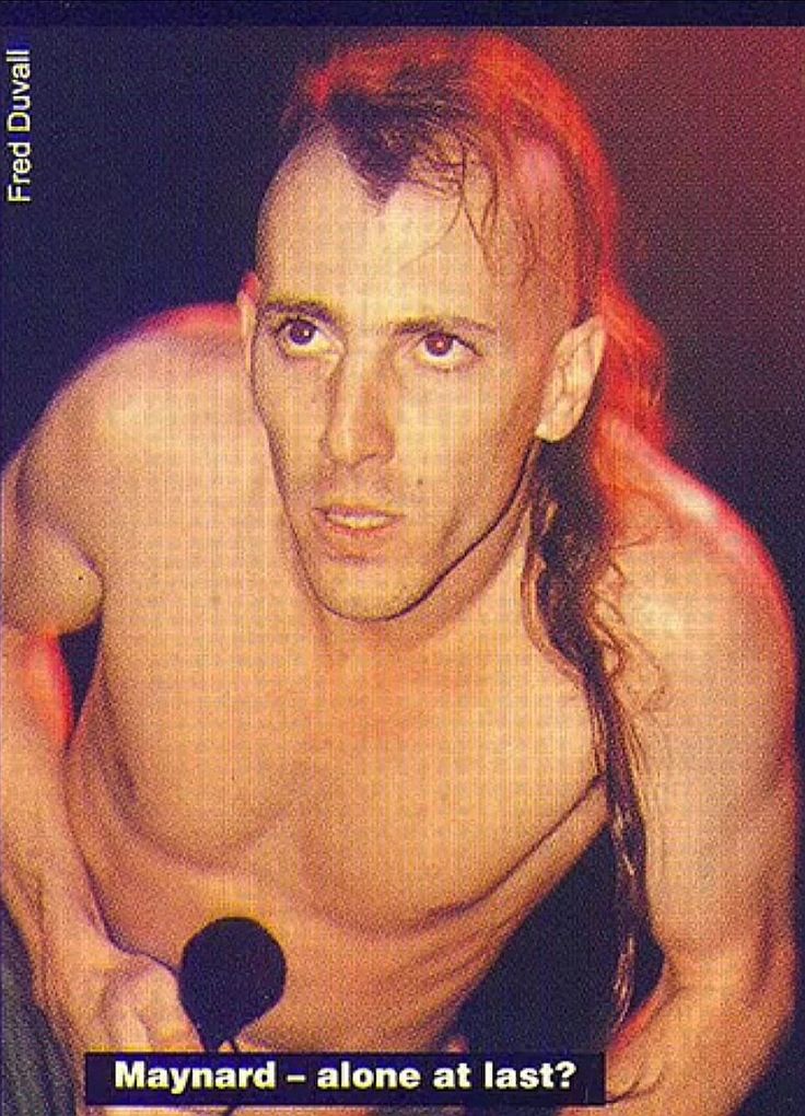 a man with long hair and no shirt on holding a microphone in his right hand