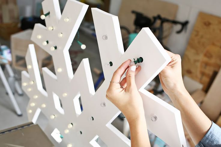 a woman is working on a snowflake made out of plywood and string lights