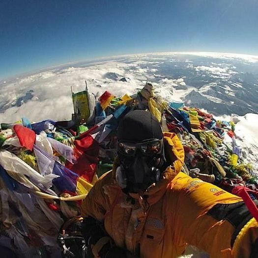 a man in yellow jacket standing on top of a mountain covered in lots of flags