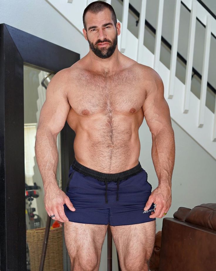 a man with no shirt standing in front of a stair case and posing for the camera