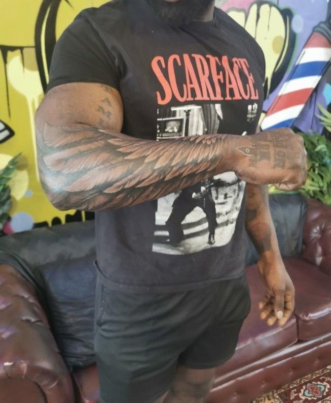 a man with tattoos on his arm standing in front of a couch