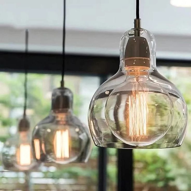 three light bulbs hanging from a ceiling in front of a window with trees and bushes