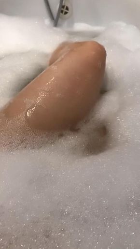 a person laying down in a bathtub filled with foam and soapy water next to a faucet