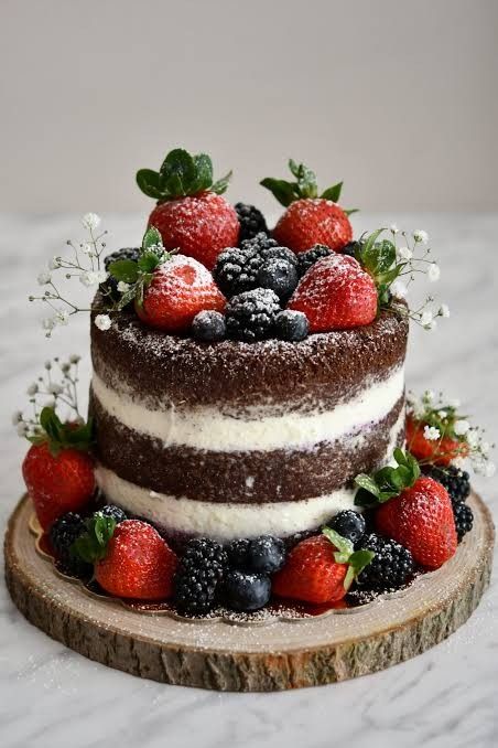 a chocolate cake with berries on top and whipped cream frosting is sitting on a wood slice