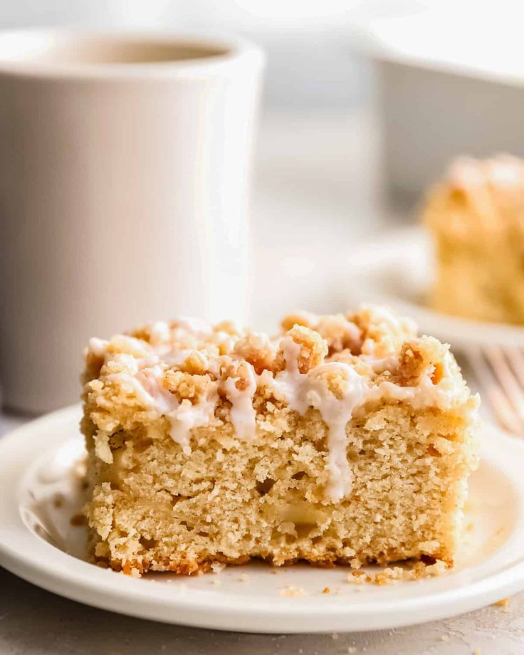 a close up of a piece of cake on a plate with a cup of coffee in the background