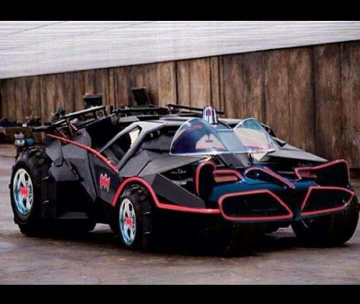 a batmobile is parked in front of a wooden wall and has red rims on it