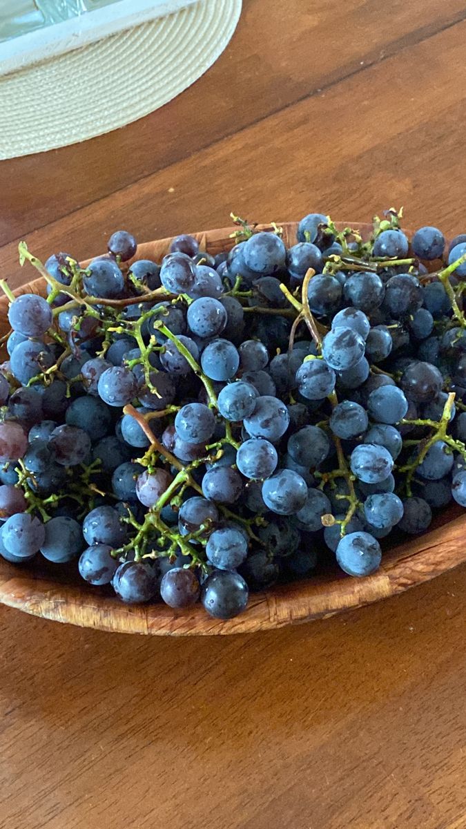 a wooden bowl filled with blue grapes on top of a table next to a plate