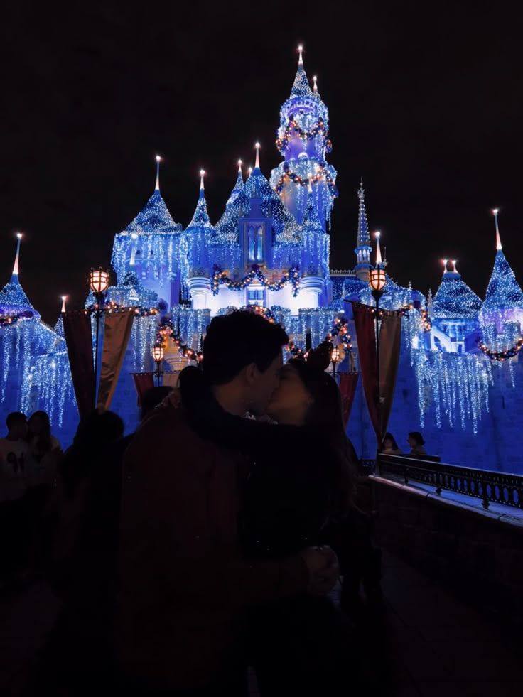 a couple kissing in front of an illuminated castle