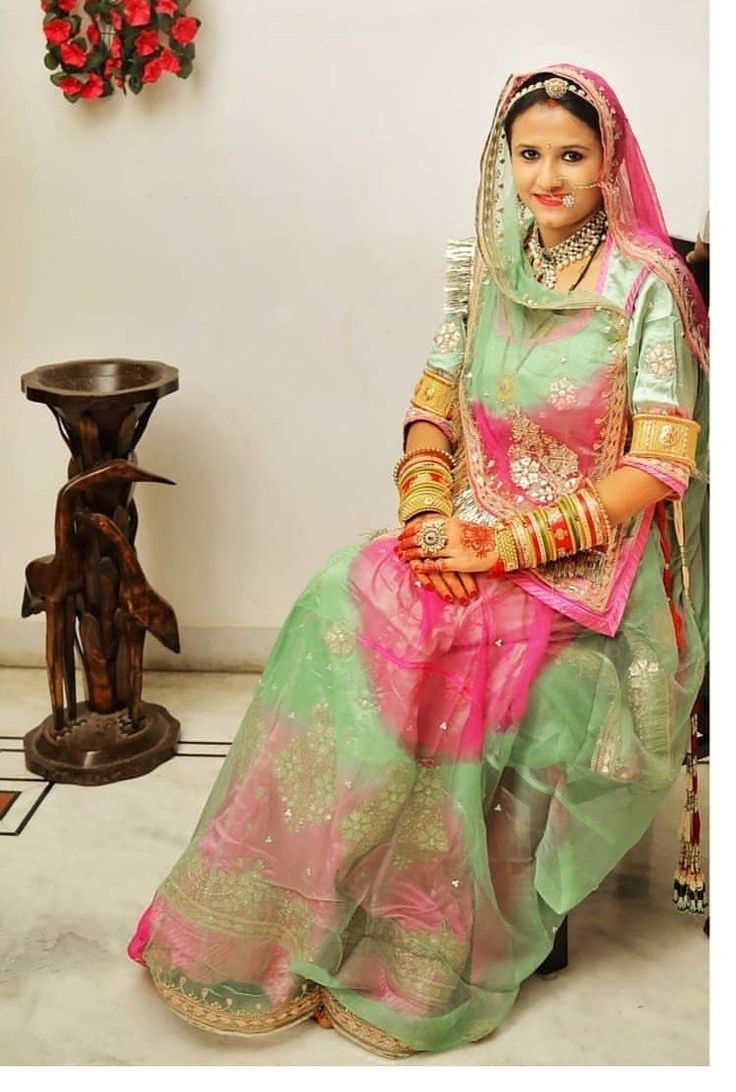 a woman in a green and pink bridal outfit sitting on a stool next to a vase