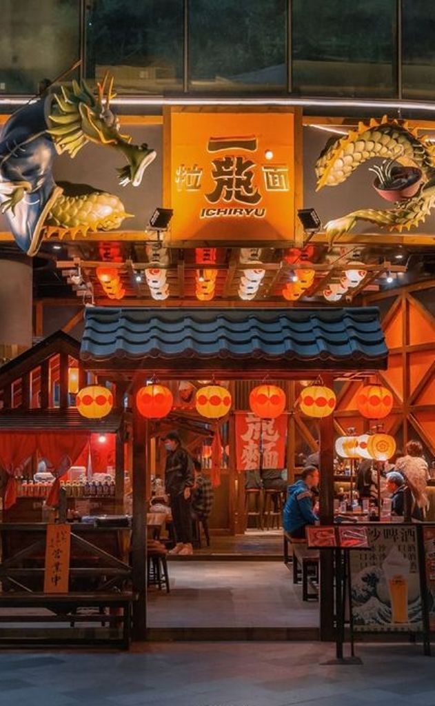 the entrance to a chinese restaurant with lanterns hanging from it's roof and people sitting at tables in front